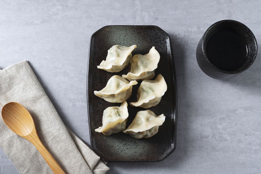 Plate of dumplings with chopsticks holding one, dipping sauce in a small bowl.
