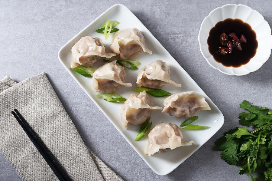 Dumplings held by chopsticks with filling visible, served with dipping sauce and scallions.
