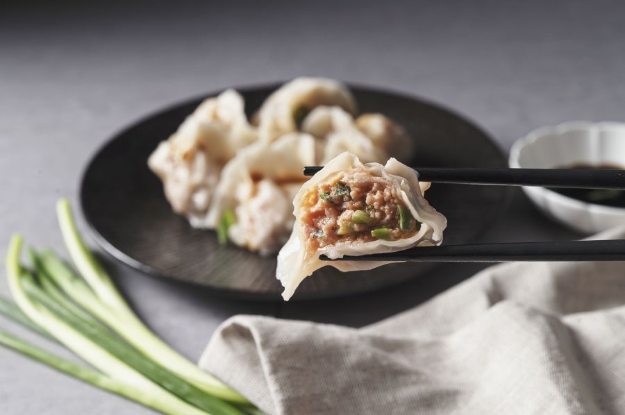 Dumplings held by chopsticks with filling visible, served with dipping sauce and scallions.
