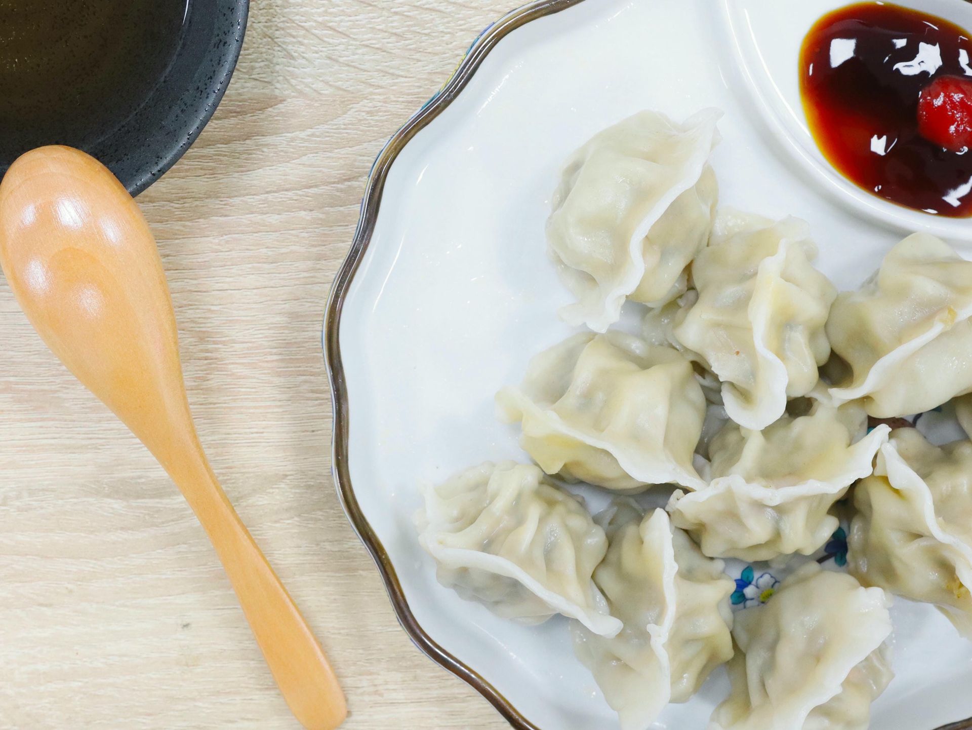 Dumpling held by golden chopsticks, revealing filling; plate of dumplings in background.