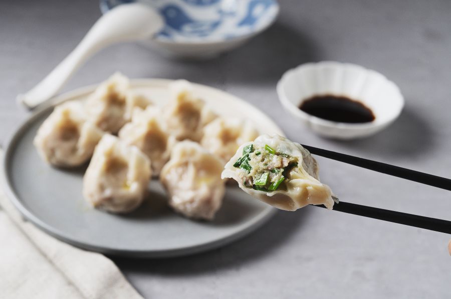 Plate of dumplings with chopsticks holding one, soy sauce, and a spoon.