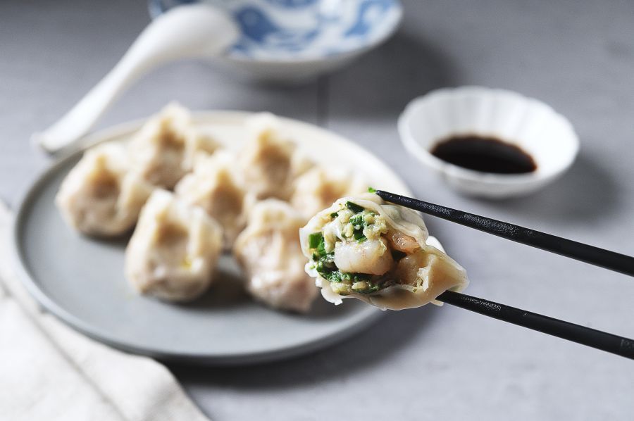 Plate of dumplings with chopsticks holding one, dipping sauce in a small bowl.