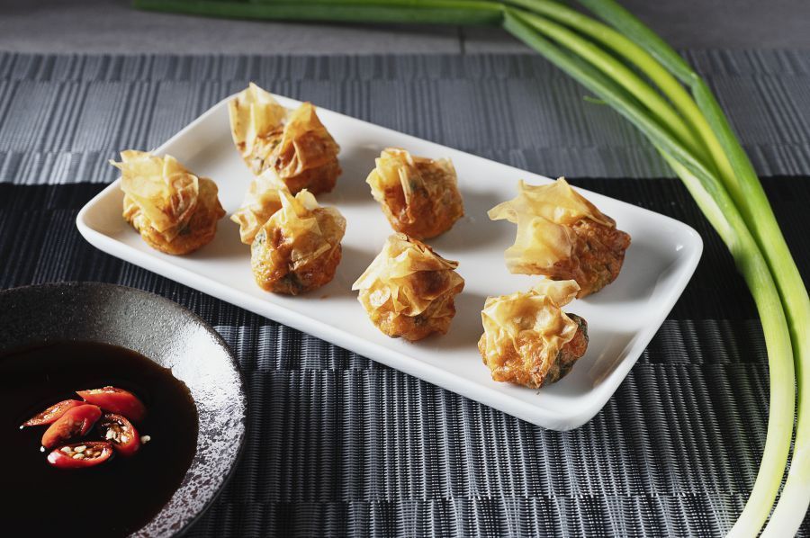 Golden fried dumplings on white plate with dipping sauce and green onions.
