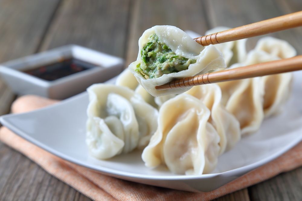 Dumplings, one held by chopsticks, on a plate, with soy sauce.
