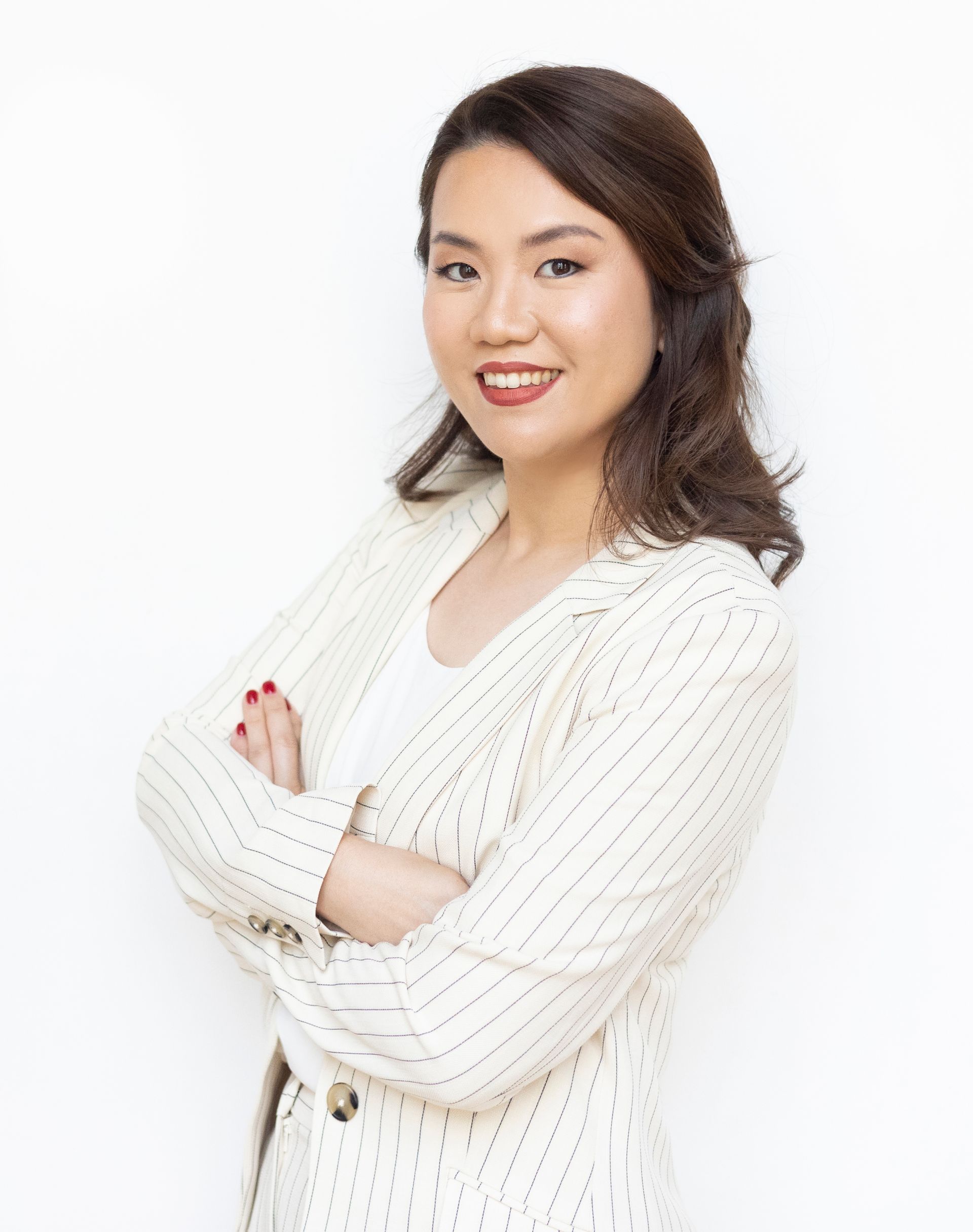 A woman in a white striped jacket is standing with her arms crossed and smiling.