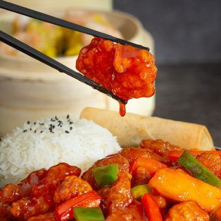 A person is holding a piece of food with chopsticks over a plate of food.