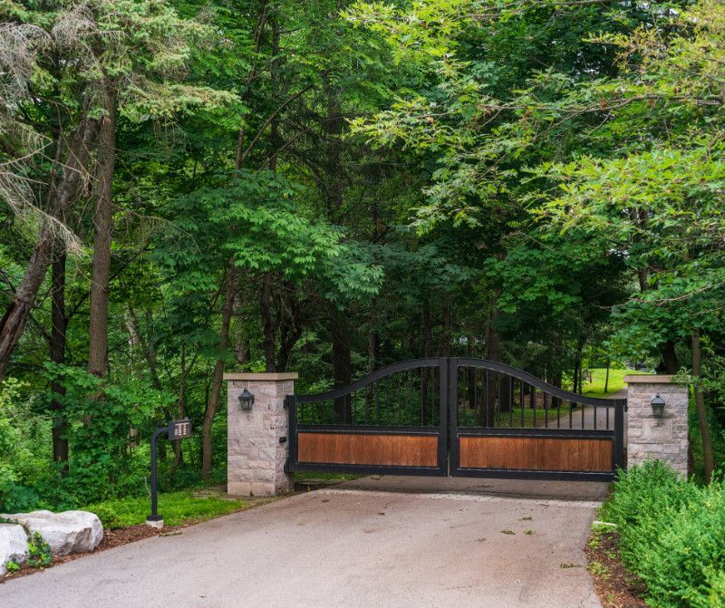 A wooden gate is leading to a driveway surrounded by trees.