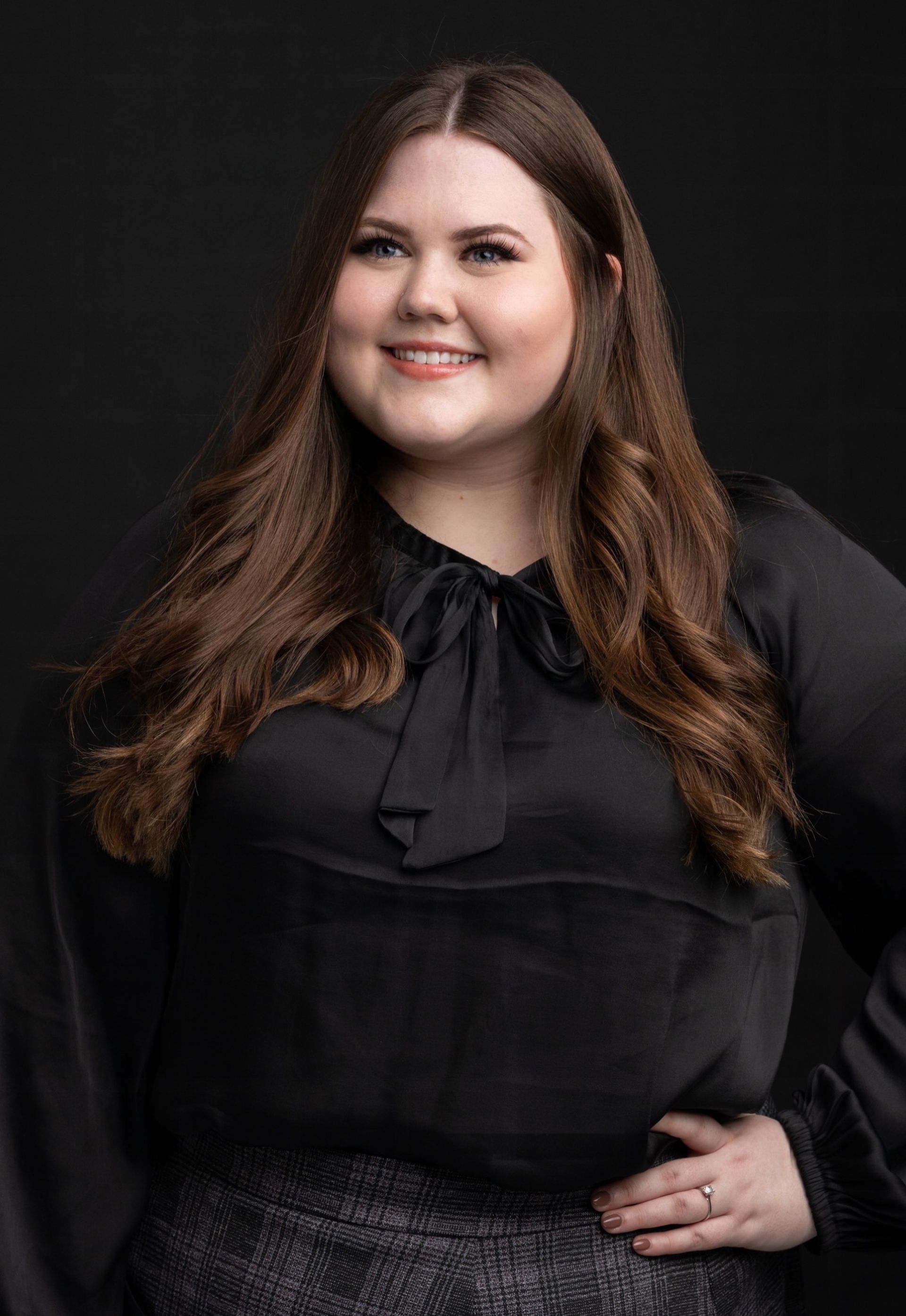 A photo of Michelle Andreacchi standing in front of a white background with a white blouse and light pink dress pants.