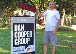 A man is holding a sold sign in front of a Dan Cooper Group for sale sign.