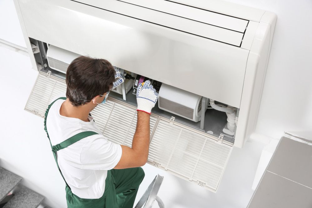 A Man Is Working on A Wall-Mounted Air Conditioner — Gordon's Air Conditioning & Refrigeration Services in Caloundra, QLD