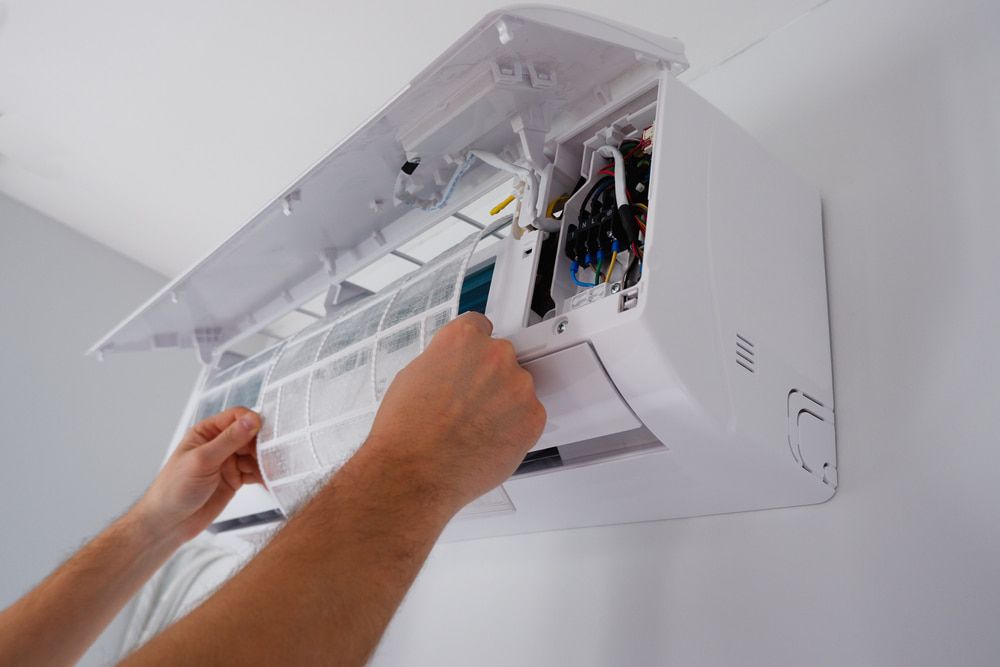 A Person Is Cleaning a Wall Mounted Air Conditioner — Gordon's Air Conditioning & Refrigeration Services in Caloundra, QLD