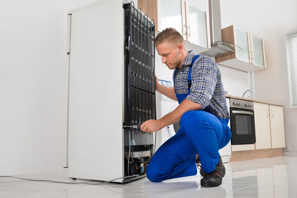 A Repairman Repairing a Refrigerator in A Kitchen — Gordon's Air Conditioning & Refrigeration Services in Caloundra, QLD