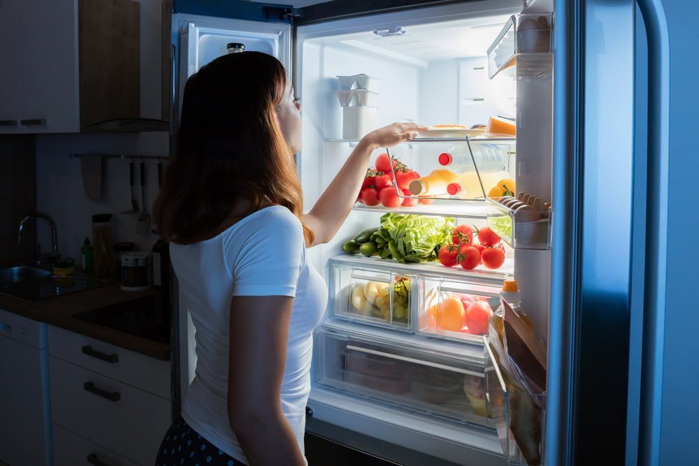 A Woman Is Taking Food out Of a Refrigerator — Gordon's Air Conditioning & Refrigeration Services in Sunshine Coast, QLD