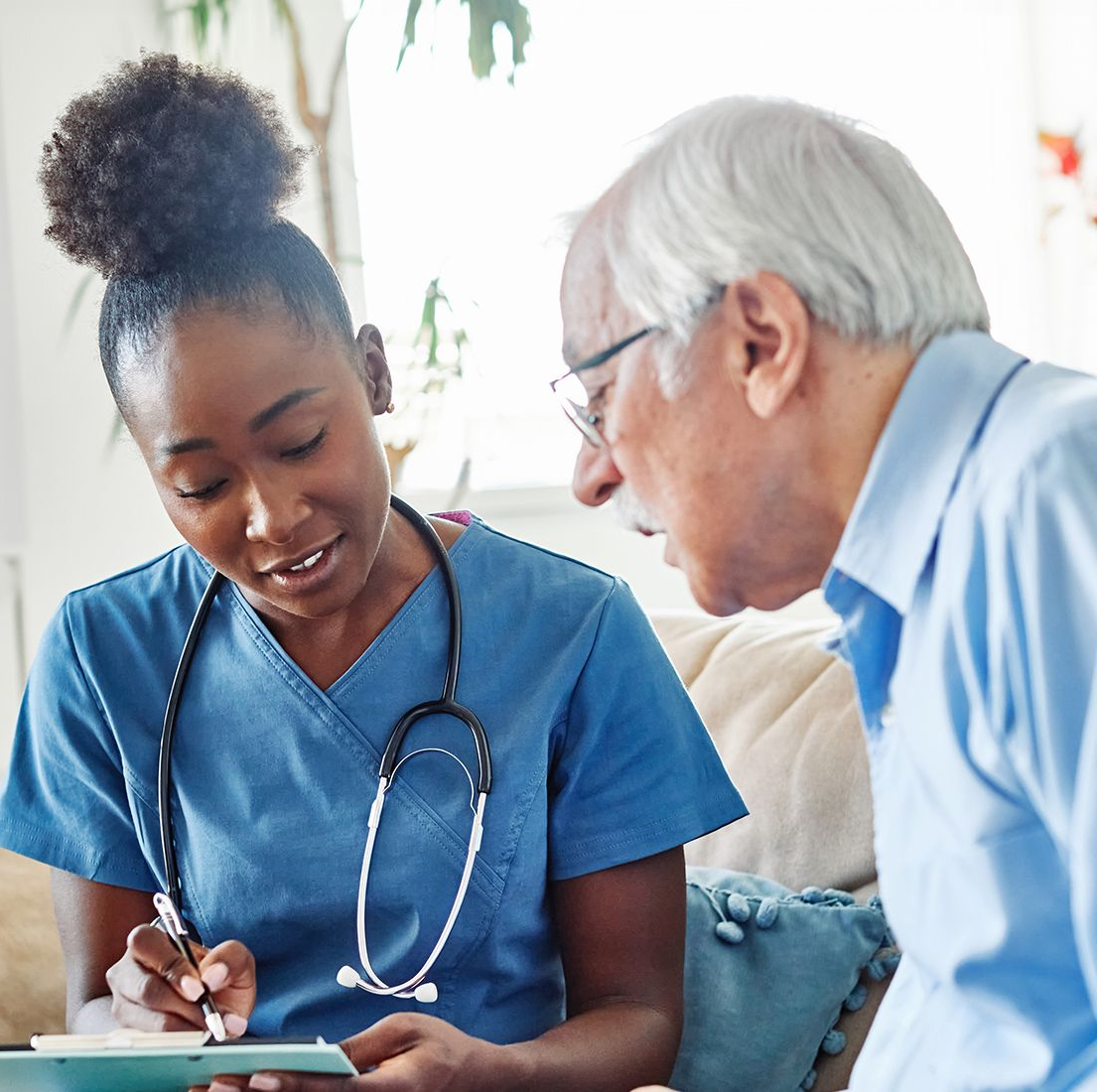 Nurse in blue scrubs reviews paperwork with patient, indoor setting.