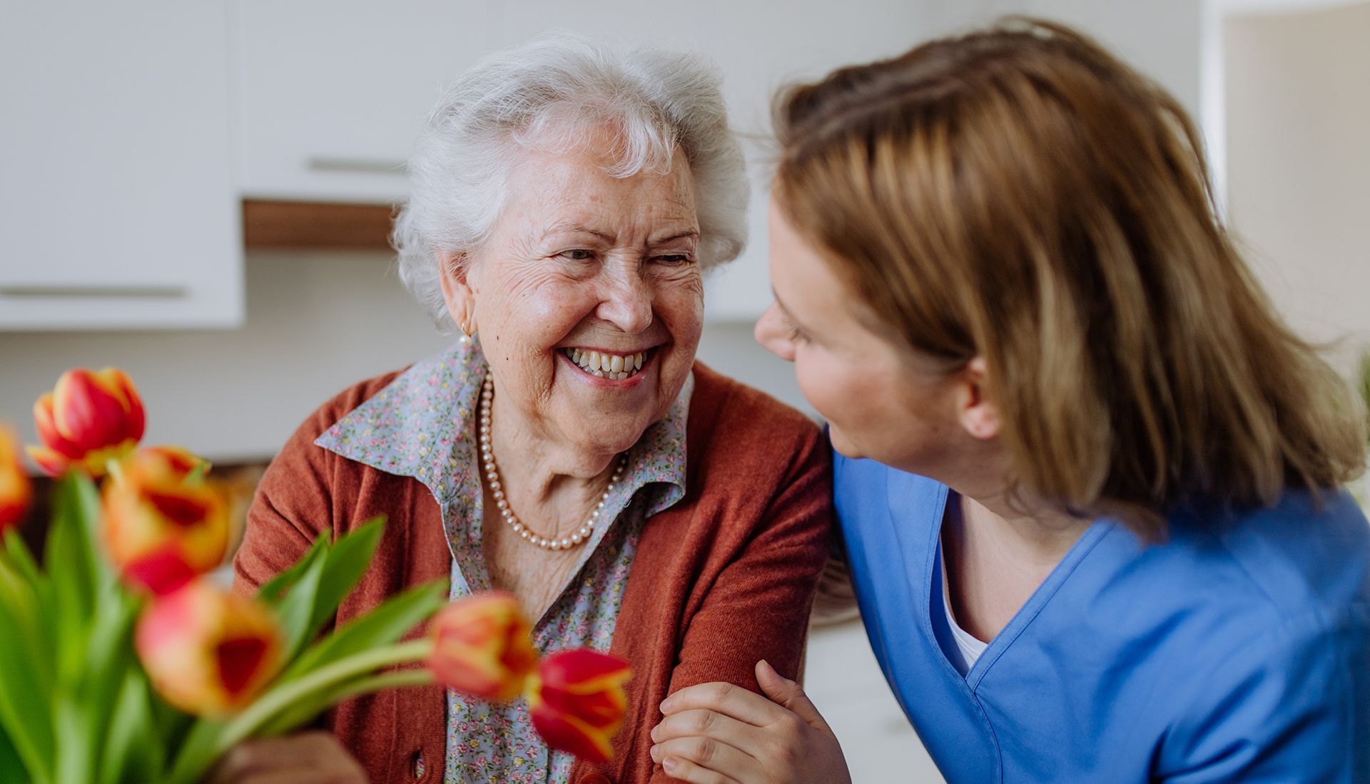 Elderly woman smiles at caregiver, with tulips in foreground.