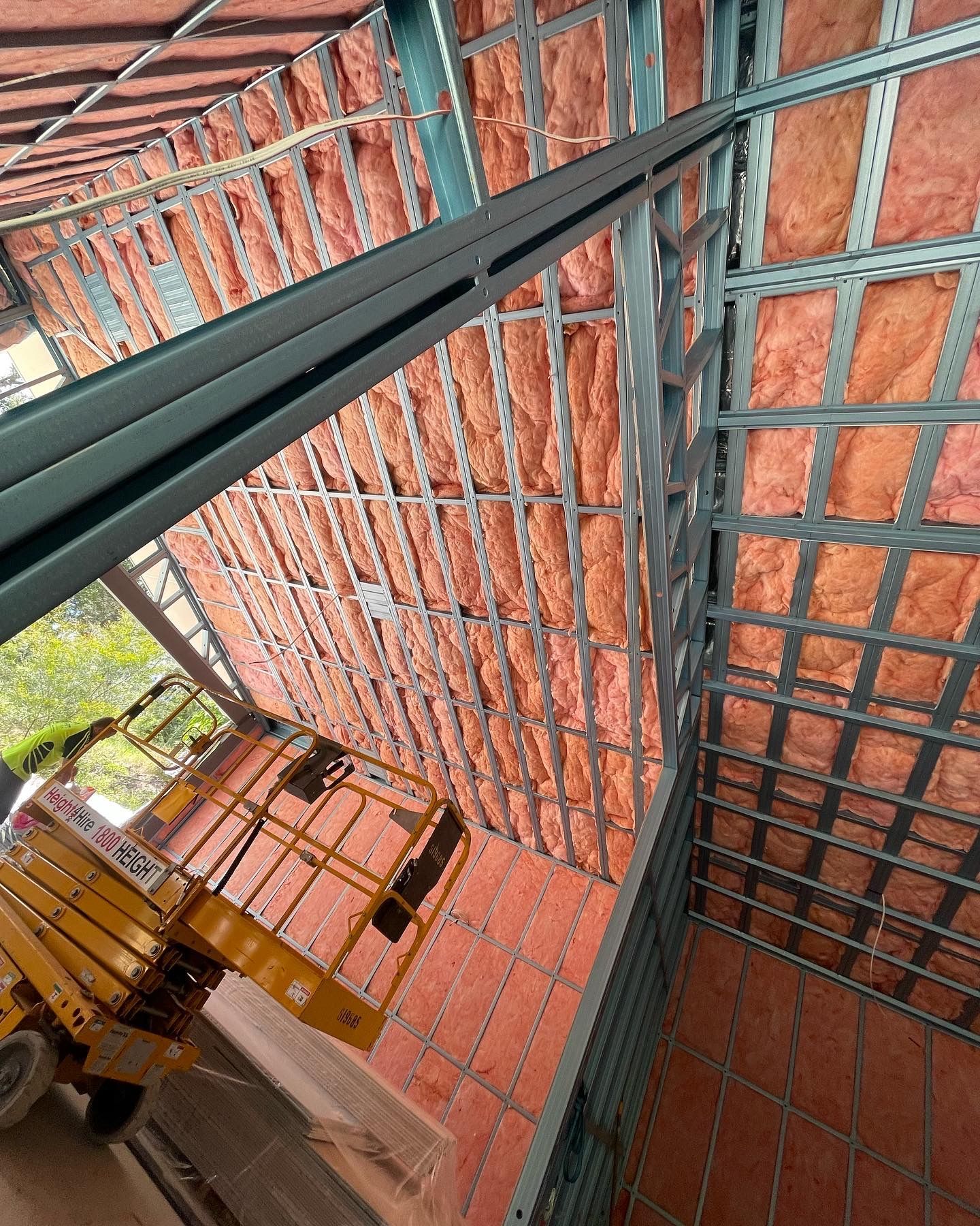 Steel framing and pink insulation in a building's roof; a yellow lift sits below.