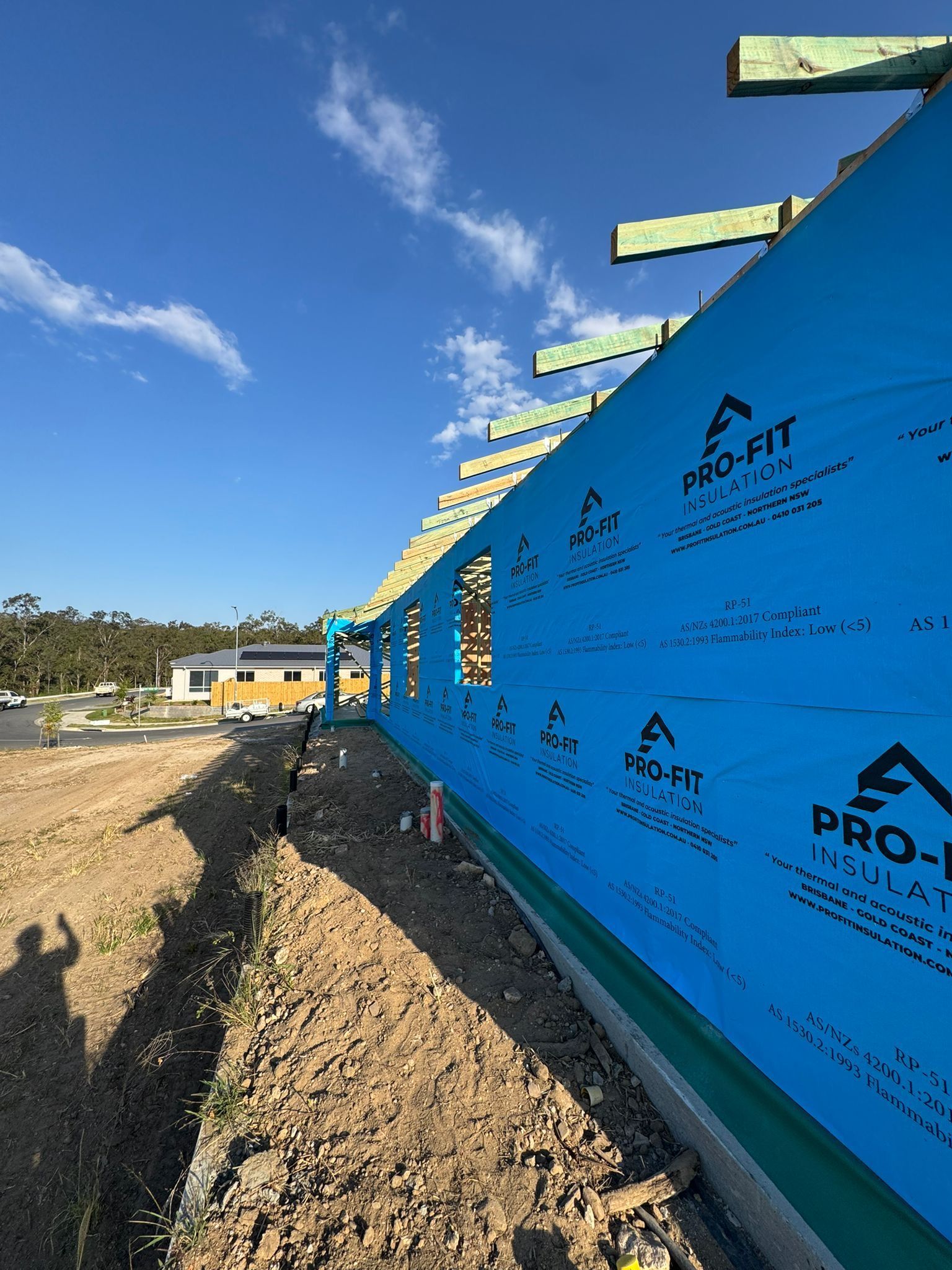 Construction site with blue protective wrap on a building's exterior, exposed rafters, and a blue sky.
