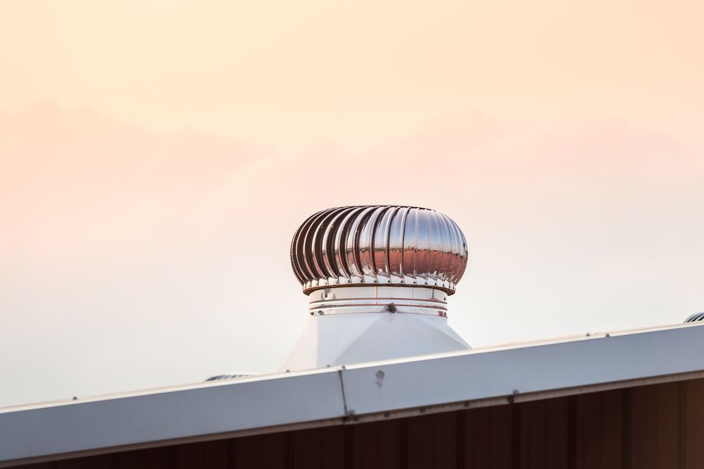A rooftop air vent with a rotating, metallic top against a pastel sky.