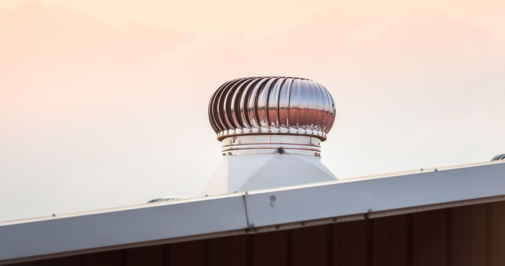 Metallic, rotating roof vent on a white rooftop against a pastel sky.