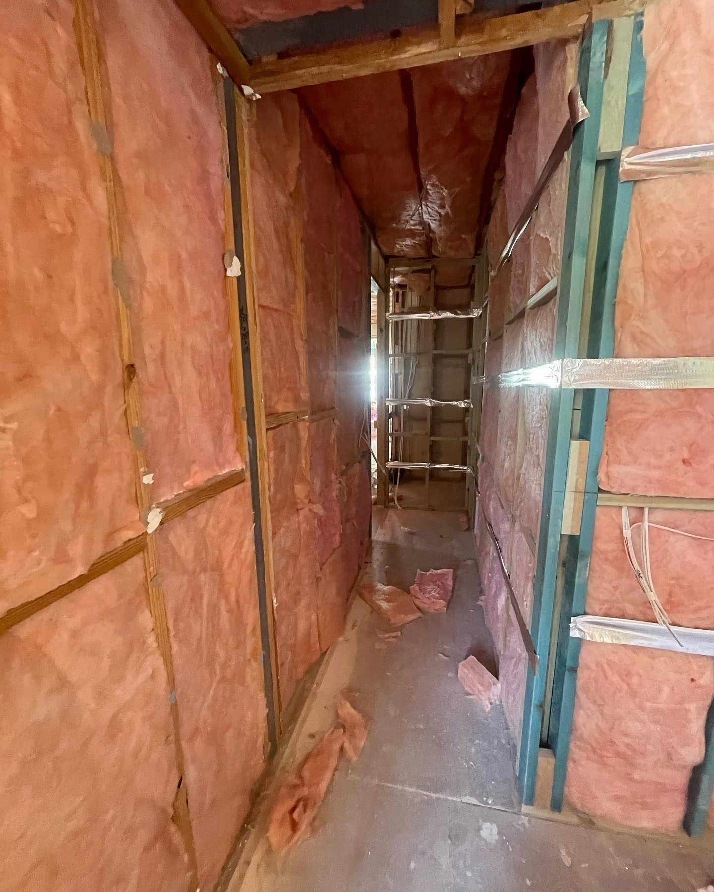 Narrow hallway with exposed wooden framing and pink insulation in the walls.