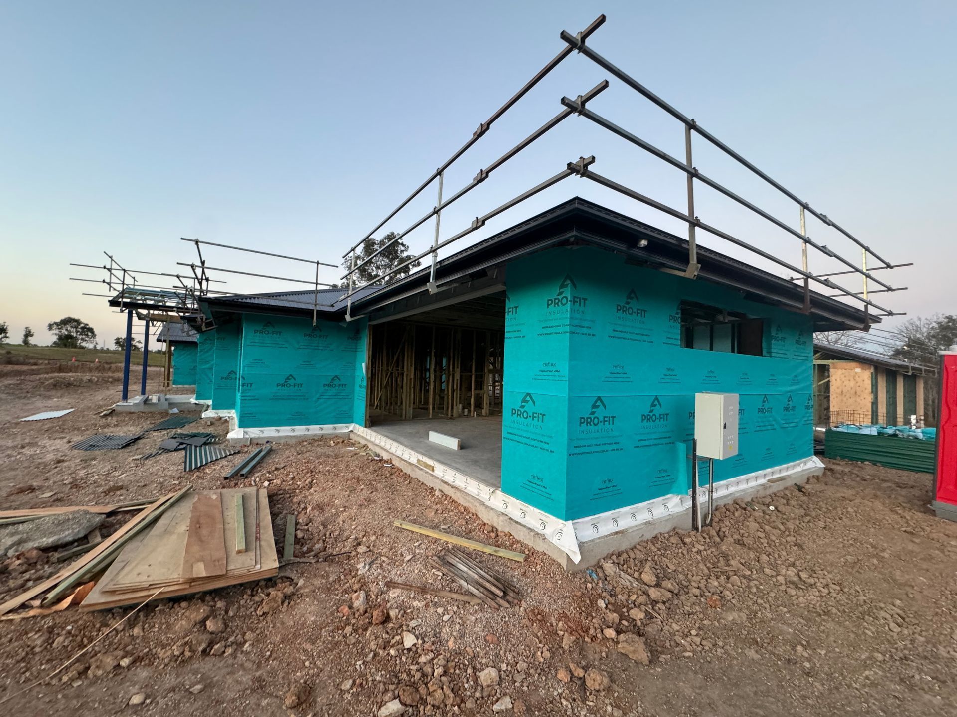 Construction site with teal sheathing, scaffolding, and concrete foundation.