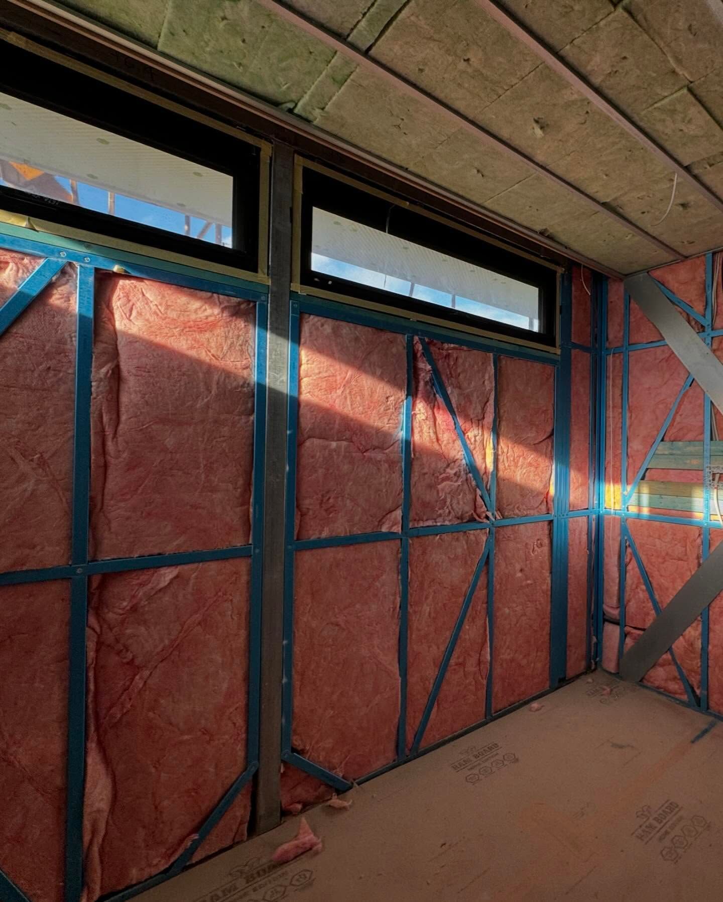 Interior construction with pink insulation between metal studs and windows.