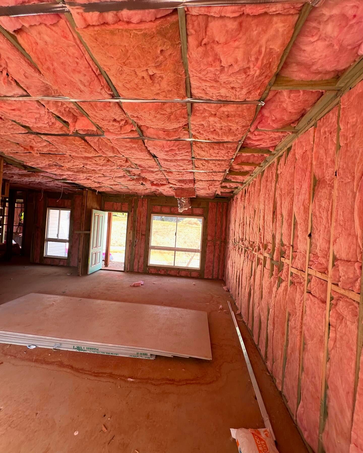 Interior of a house under construction with pink insulation on the walls and ceiling.