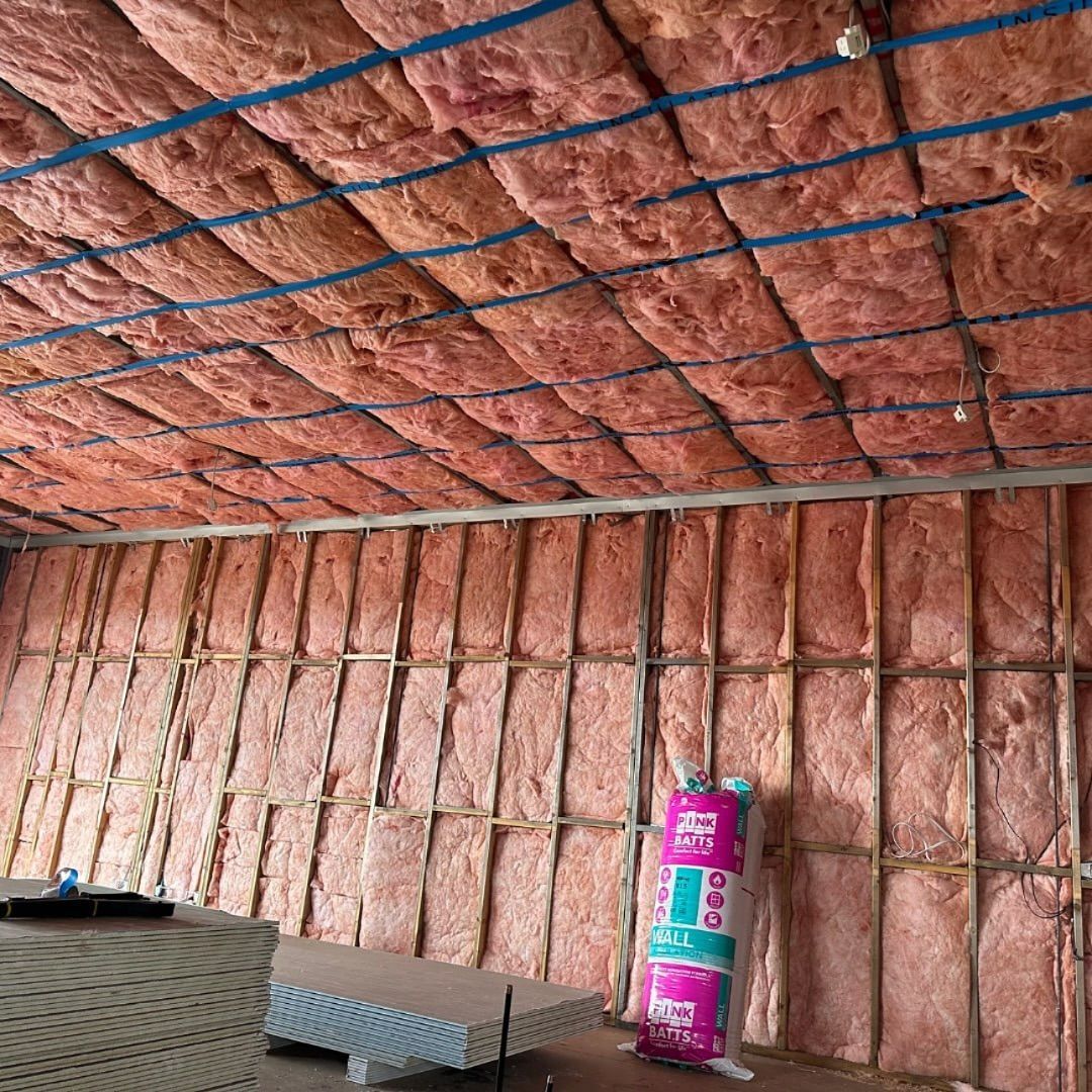 Pink insulation installed in the ceiling and walls of a room. Blue straps secure ceiling insulation.