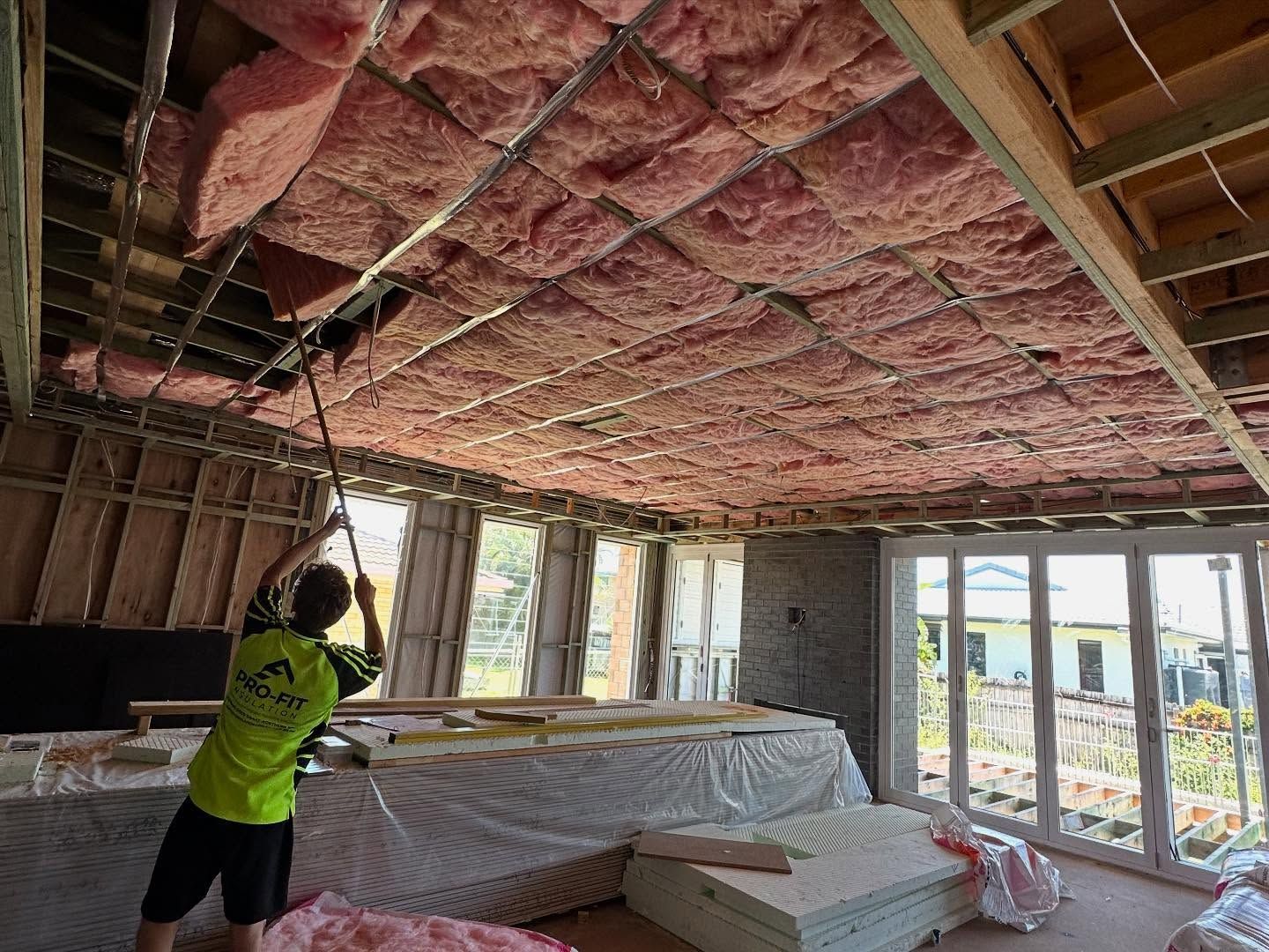 Man installing pink insulation in a ceiling during construction, interior view.