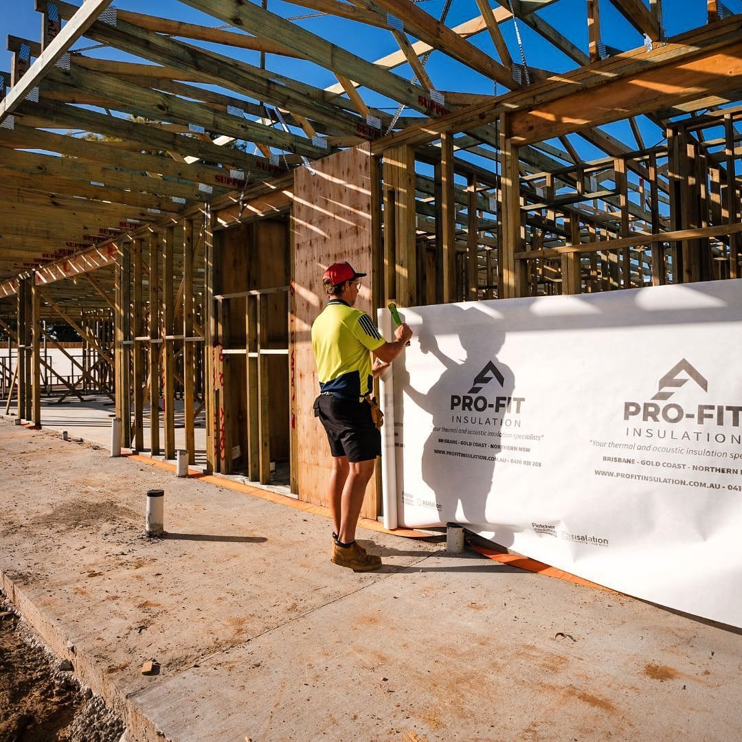 Construction worker installing Pro-Fit weather barrier on a wood frame building. Sunny day.