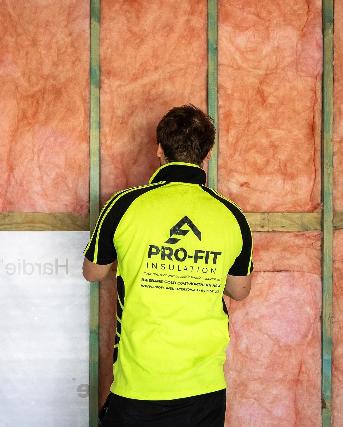 Man in yellow shirt installs insulation between wooden wall studs.