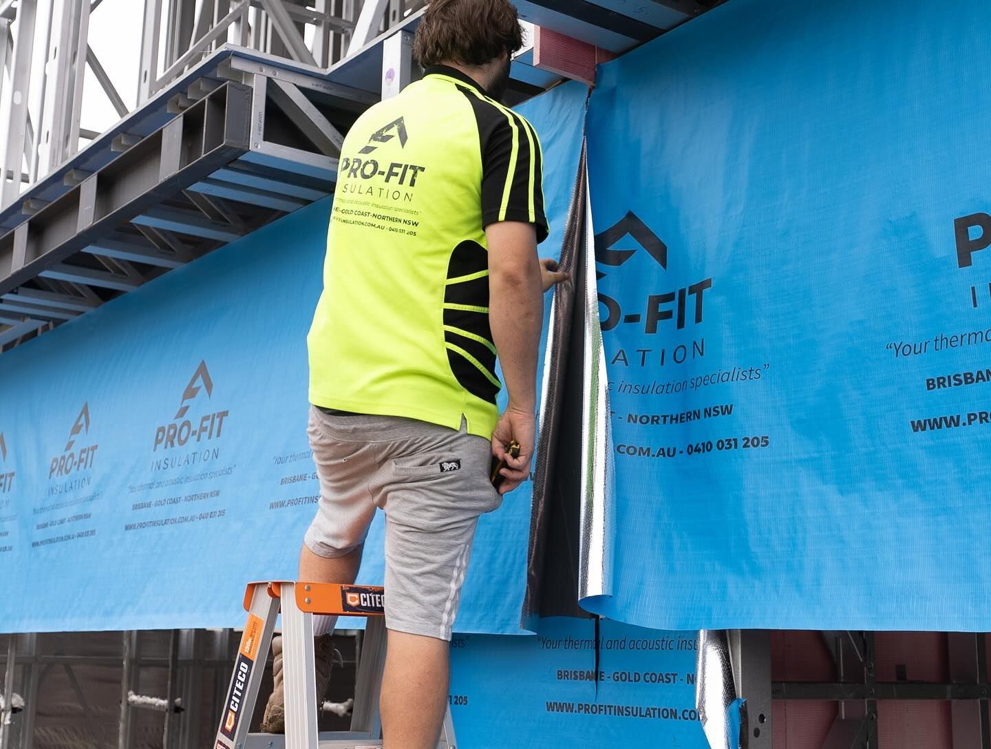 Construction worker installing blue insulation on a building exterior.