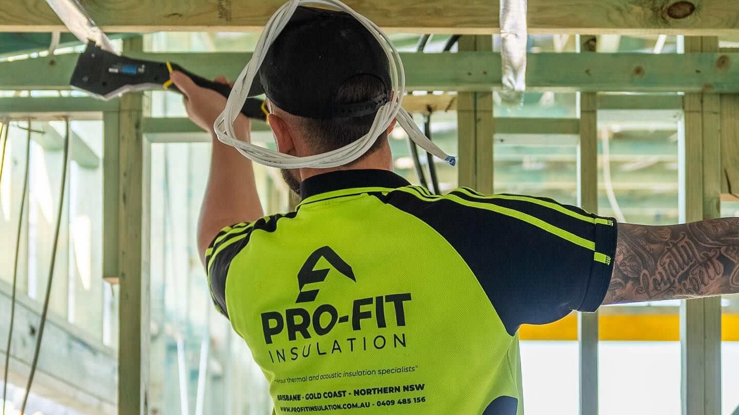 Man in neon shirt installing insulation in a wood-framed structure.