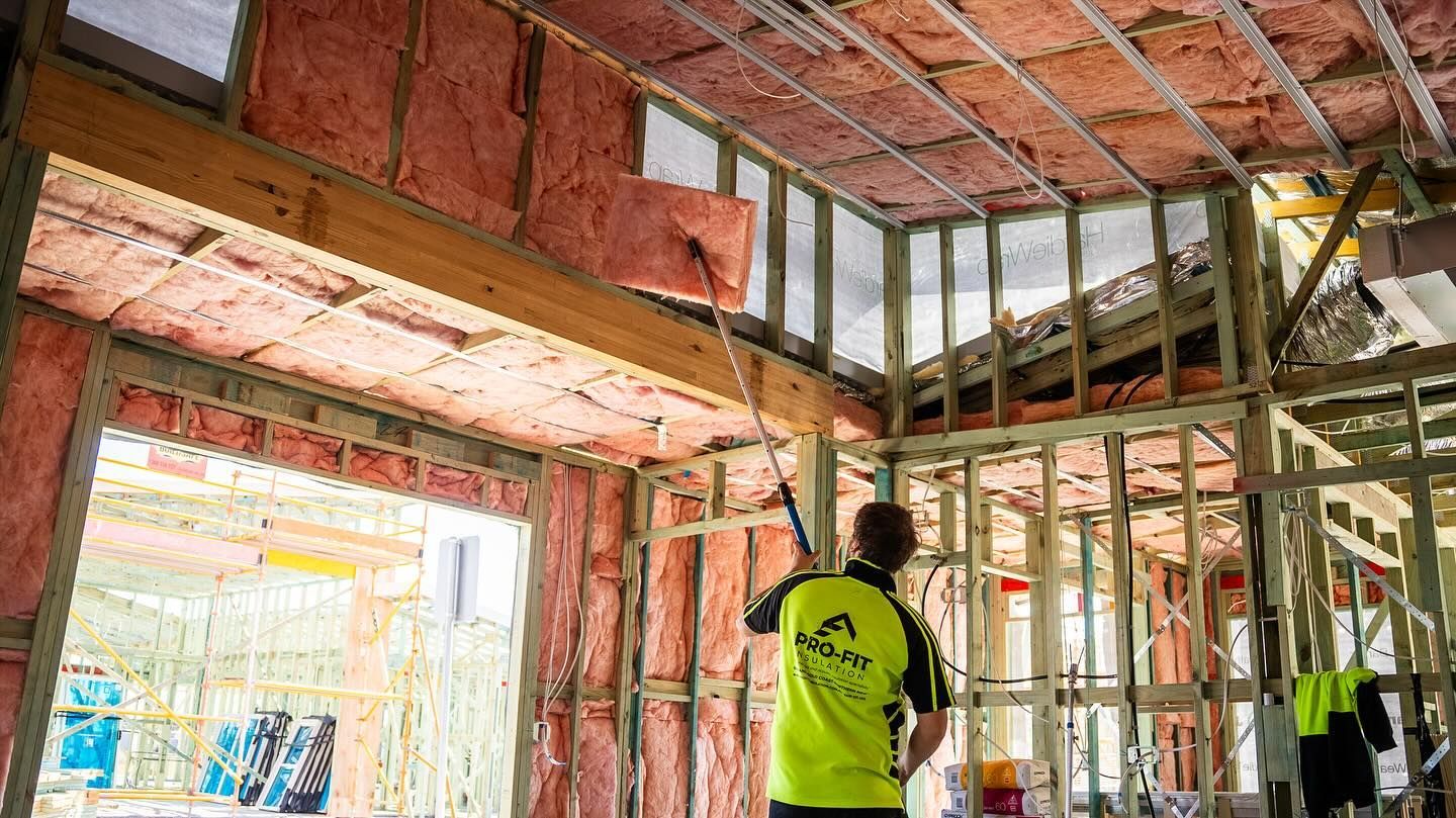 Construction worker installing pink insulation in a house frame.