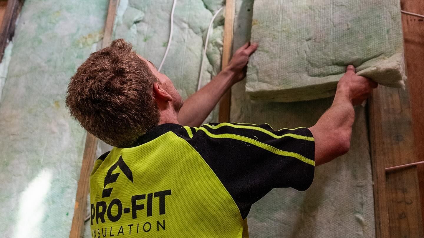 Person installing insulation in a wall, wearing a yellow and black shirt.