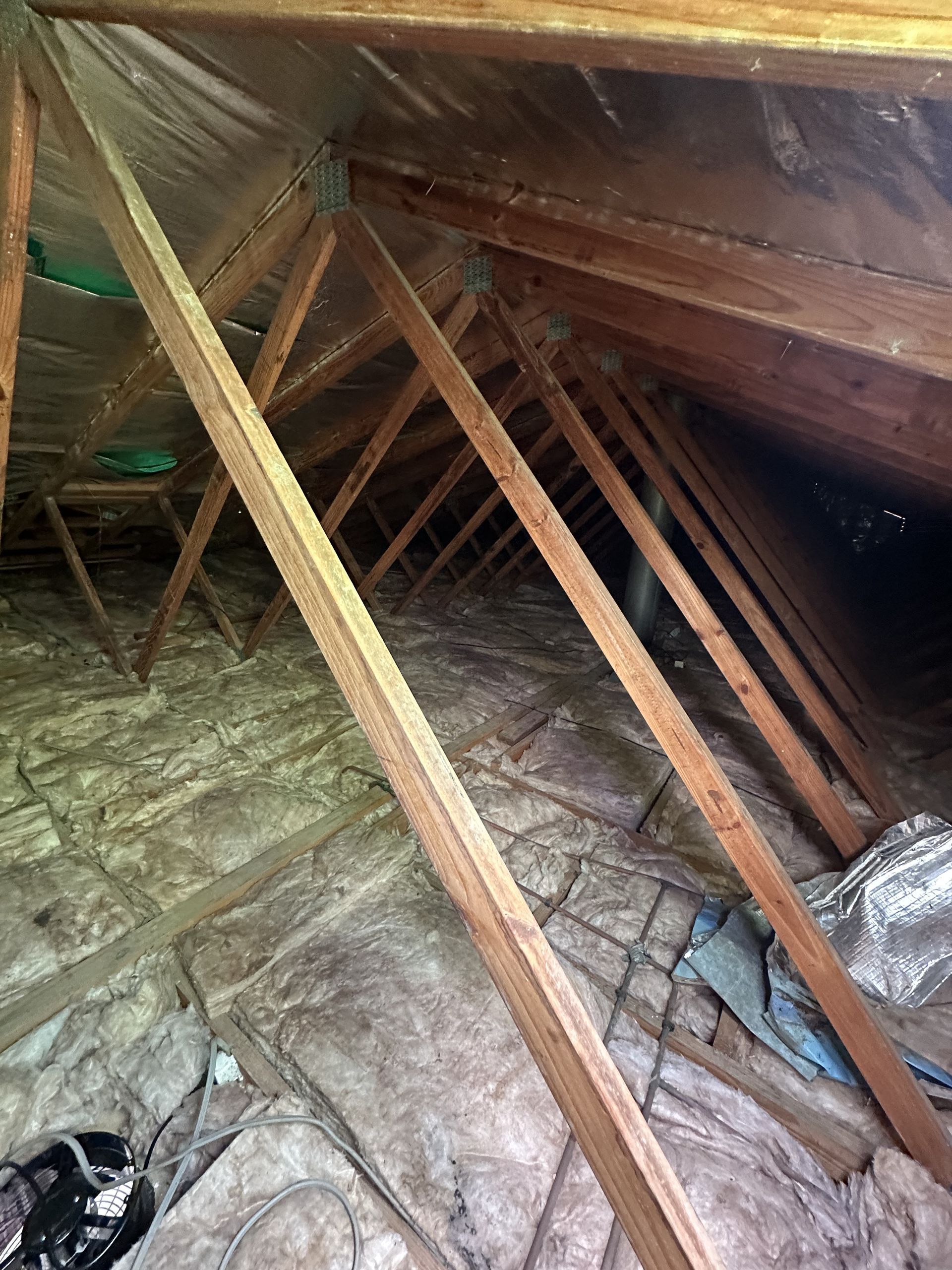 Interior of an attic with wooden rafters and insulation on the floor and sides.