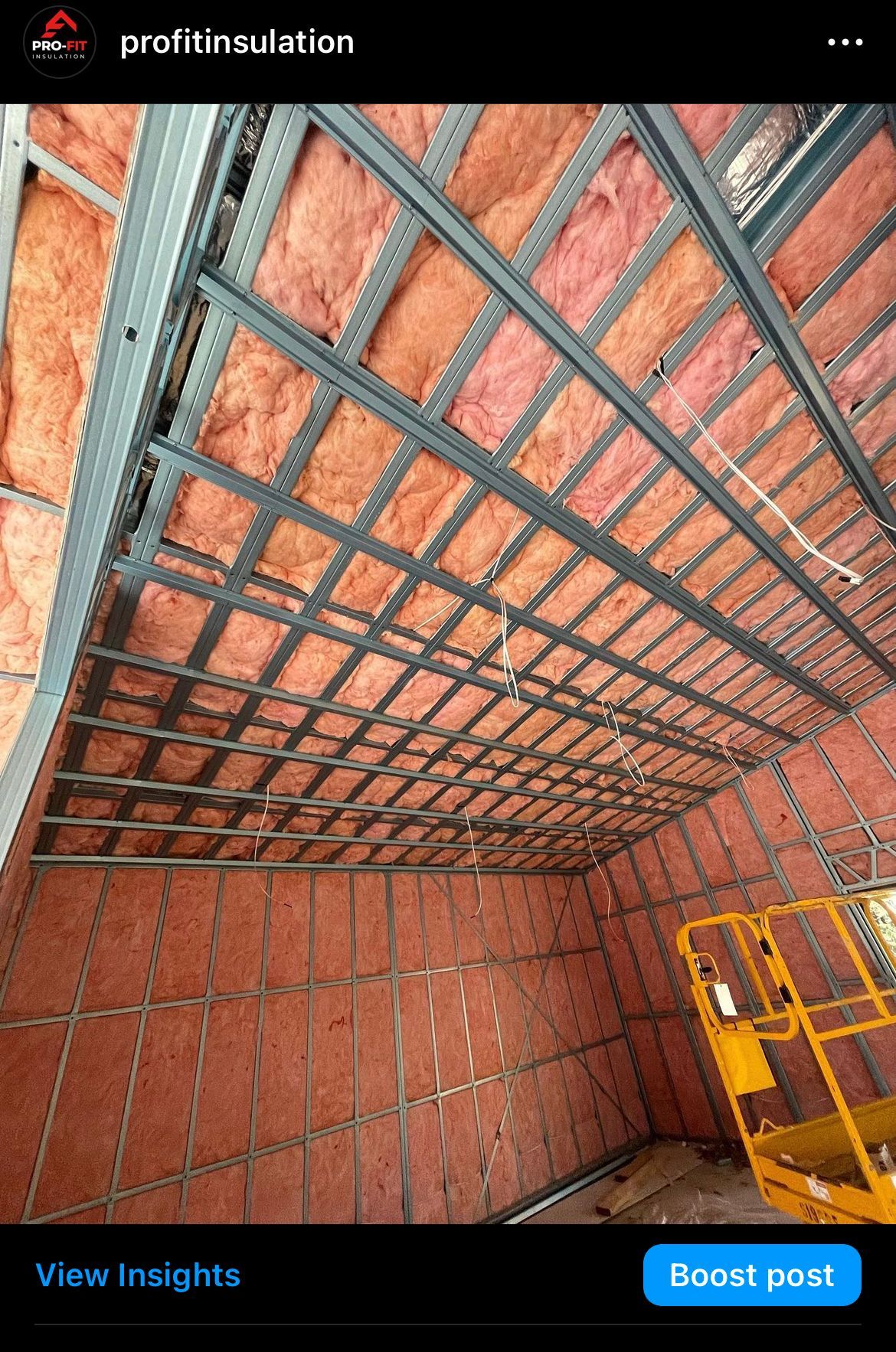 Interior with pink insulation between metal framing. A yellow lift is in the corner.