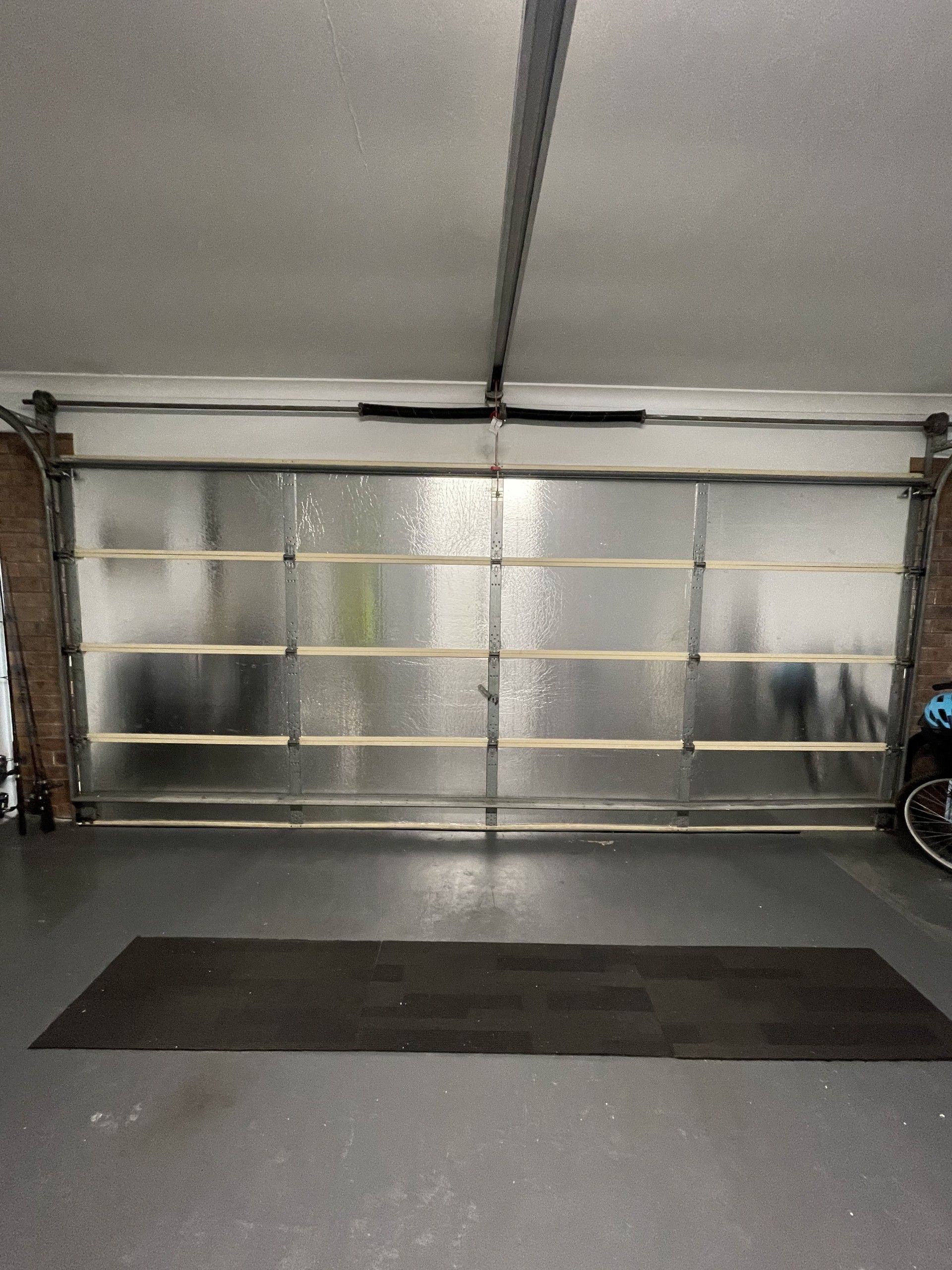 Garage with a closed, frosted-glass door, a dark mat on the floor, and grey walls.