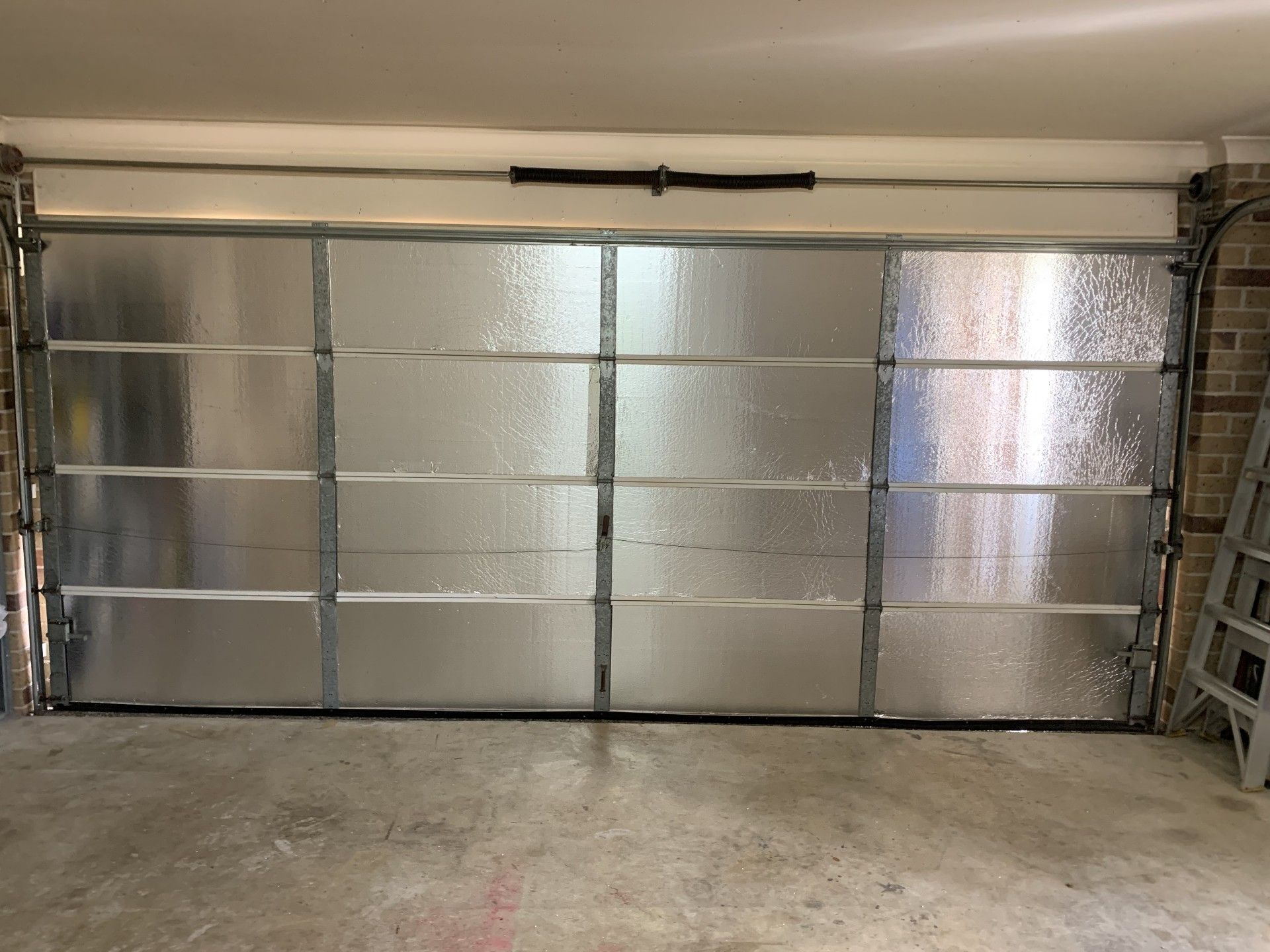 Insulated garage door, closed. Silver panels, metal frame. Interior view, concrete floor.