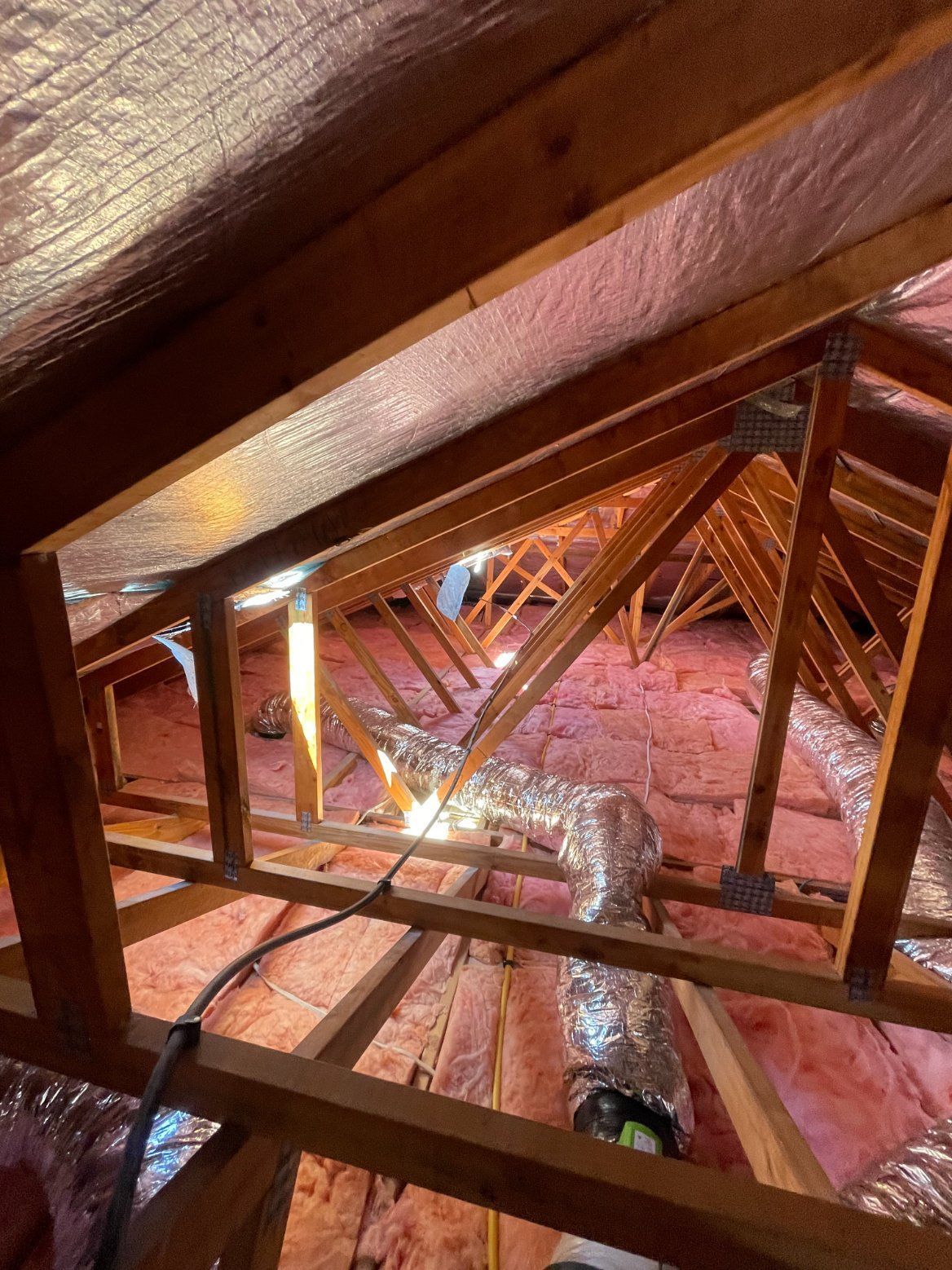 Attic interior with exposed wooden rafters, pink insulation, and silver ductwork.