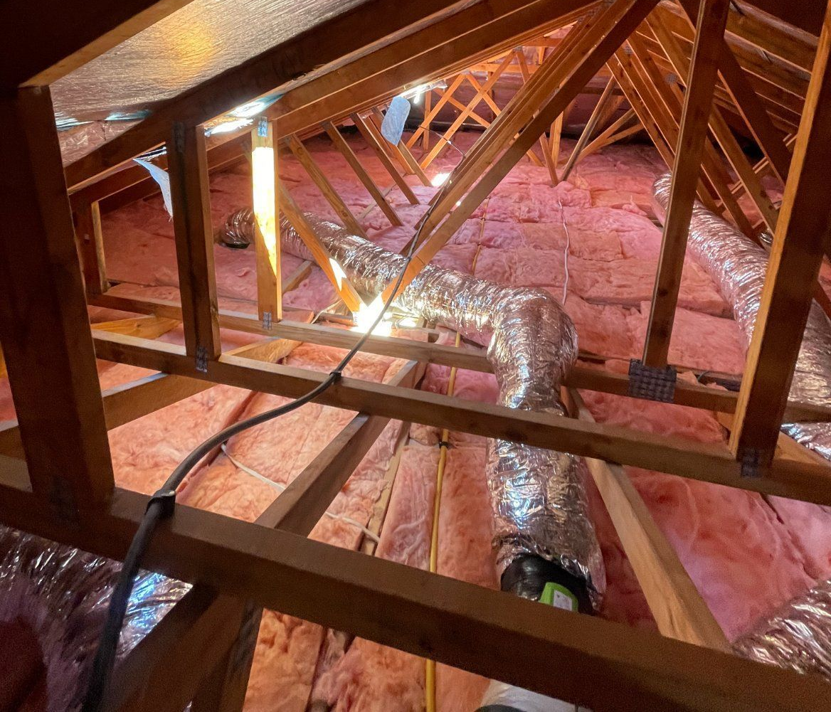 Attic interior with pink insulation, wooden beams, and silver air ducts.