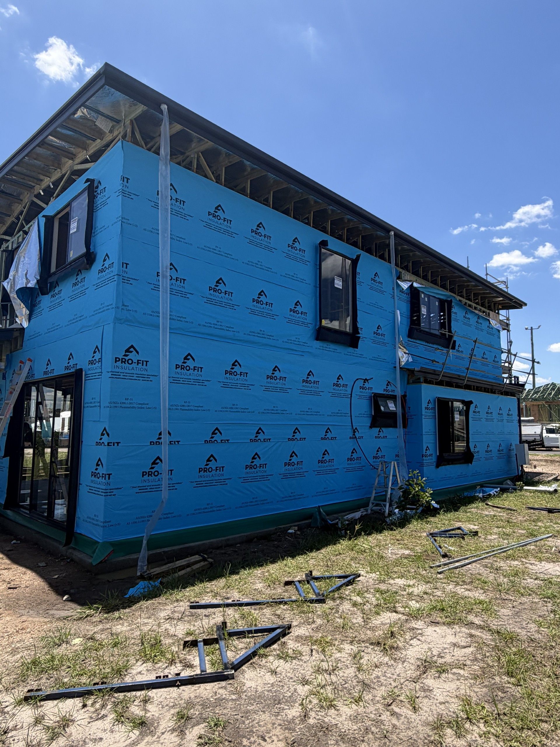 Two-story house under construction with blue weather barrier and black window frames.
