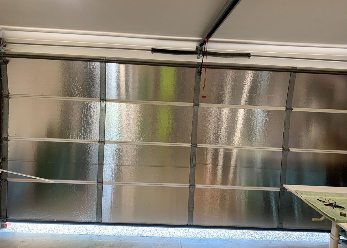 Insulated garage door, closed. Reflective silver panels. Overhead track and spring visible.