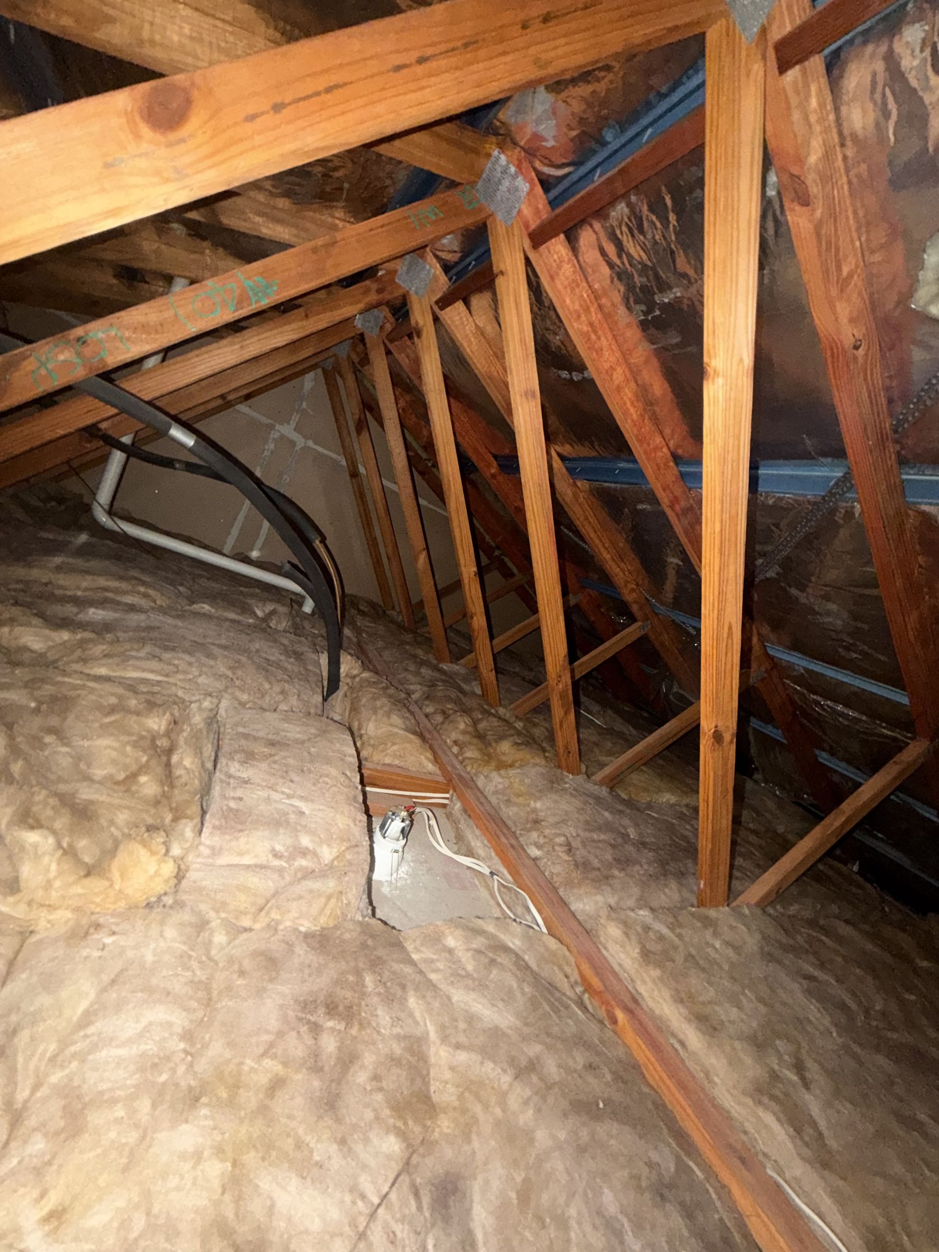 Interior view of a dusty attic with wooden beams, insulation, and electrical wiring.