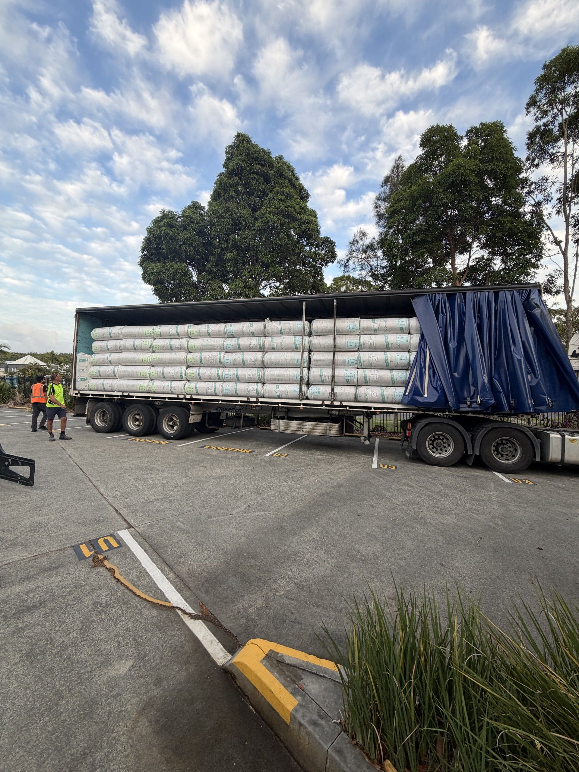 Construction worker installing insulation in a new building frame; pink insulation, wood beams.