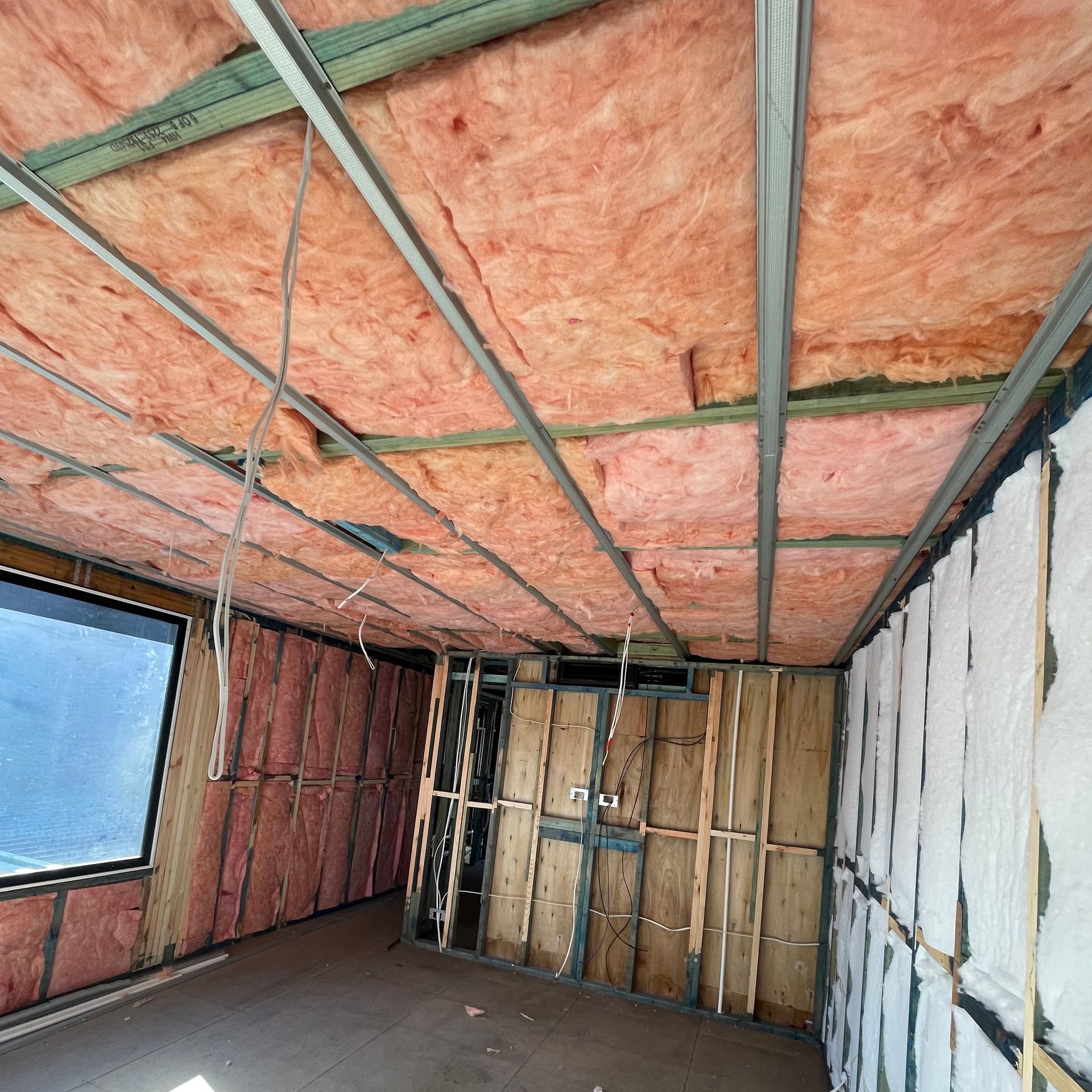 Interior view of a room under construction with exposed insulation in the ceiling and walls.