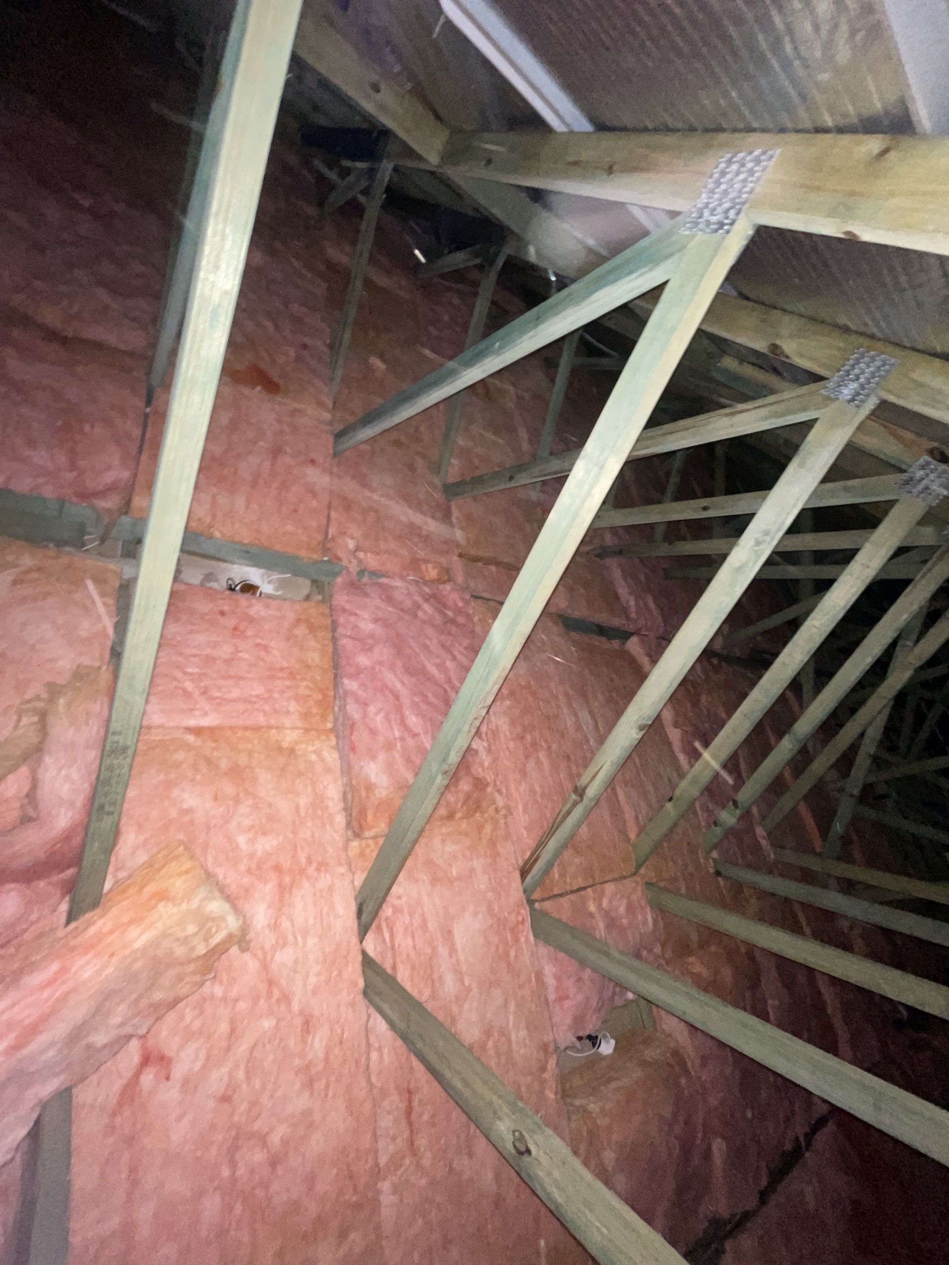 Attic interior showing pink insulation between wooden rafters and beams.