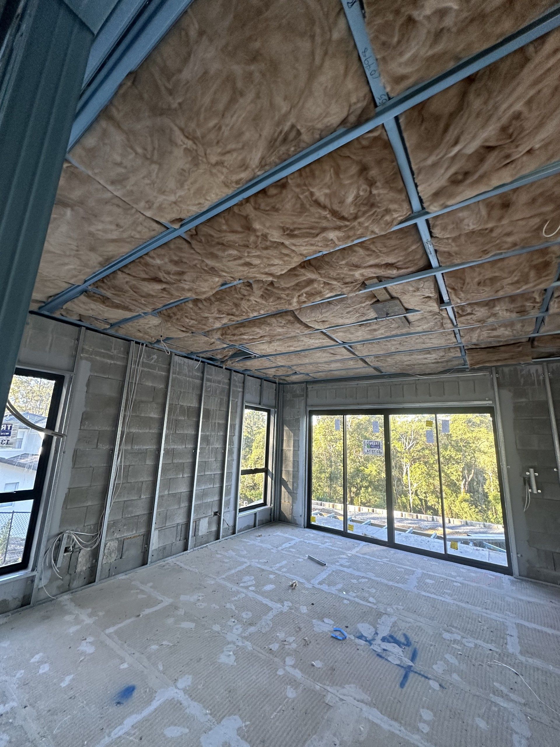 Interior of a room under construction, with exposed insulation in the ceiling and concrete walls.