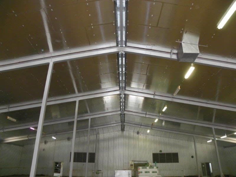 Interior of a large metal building with overhead lighting and reflective panels.