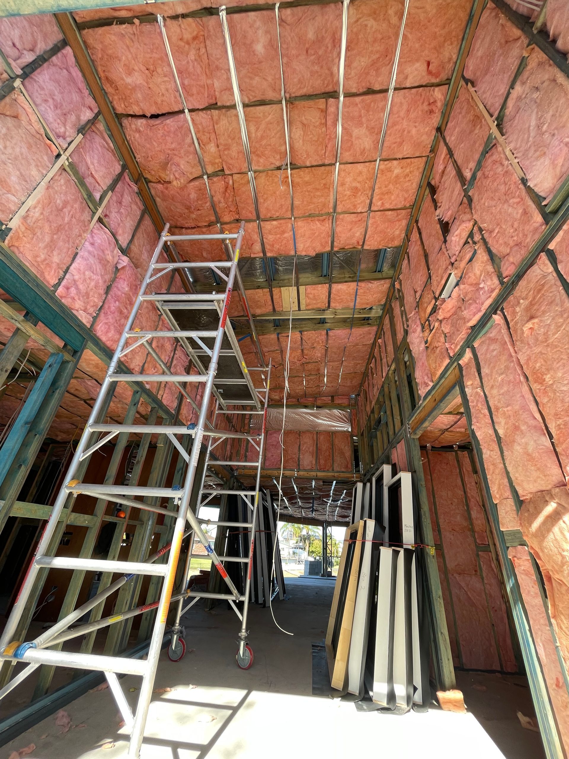 Interior construction with pink insulation, scaffolding, and framing.